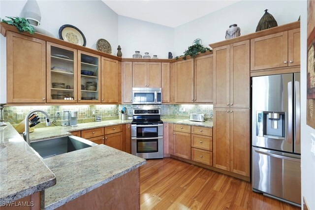 kitchen with light stone countertops, sink, decorative backsplash, appliances with stainless steel finishes, and light wood-type flooring