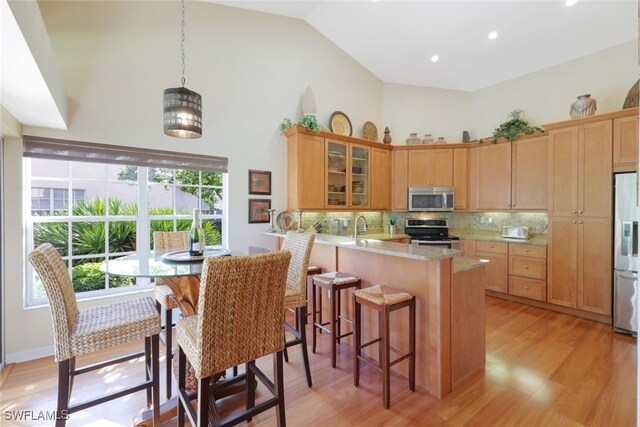 kitchen featuring kitchen peninsula, appliances with stainless steel finishes, decorative backsplash, light hardwood / wood-style floors, and hanging light fixtures