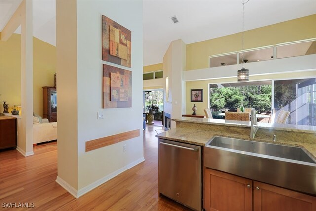 kitchen with light stone countertops, plenty of natural light, stainless steel dishwasher, and light wood-type flooring