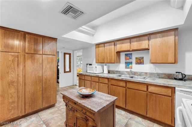 kitchen with light tile patterned floors, white appliances, a kitchen island, and sink