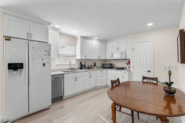 kitchen with light stone counters, white appliances, sink, light hardwood / wood-style floors, and white cabinetry