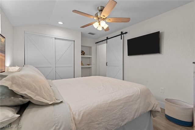 bedroom with light wood-type flooring, a closet, vaulted ceiling, ceiling fan, and a barn door