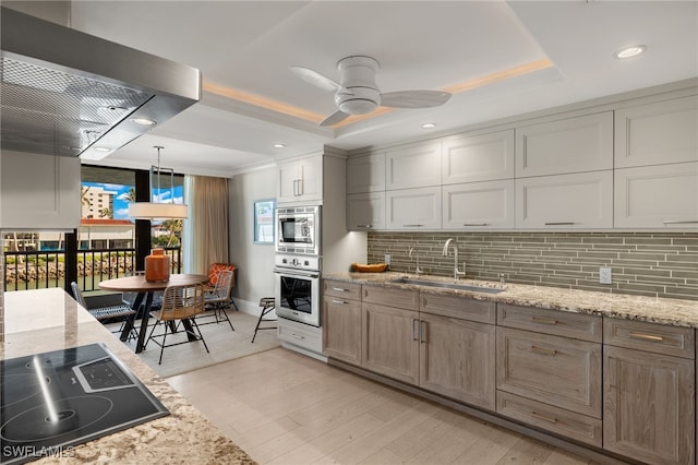 kitchen featuring oven, sink, black electric cooktop, decorative light fixtures, and light stone counters