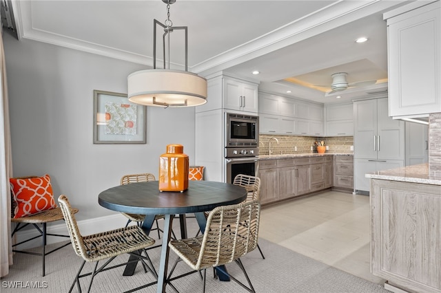 dining space with a tray ceiling, ceiling fan, ornamental molding, and sink