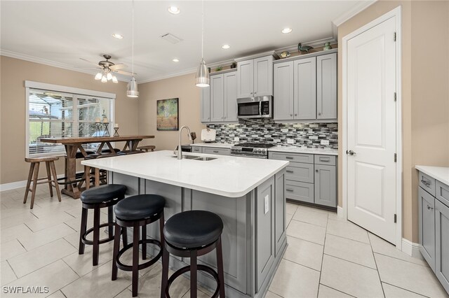 kitchen featuring gray cabinets, light countertops, appliances with stainless steel finishes, a sink, and an island with sink