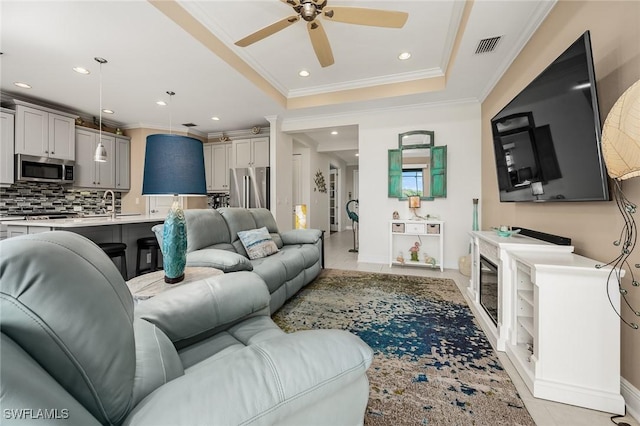 living room featuring light tile patterned floors, a ceiling fan, a tray ceiling, crown molding, and recessed lighting