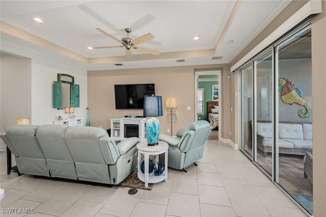 living room with light tile patterned floors, a ceiling fan, a tray ceiling, and crown molding