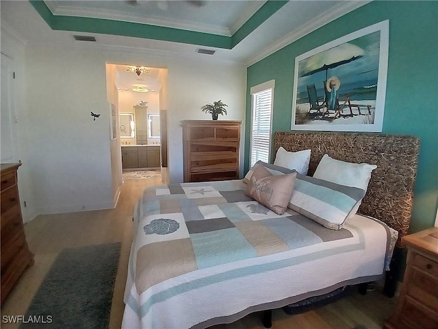 bedroom featuring ensuite bathroom, wood finished floors, visible vents, ornamental molding, and a tray ceiling