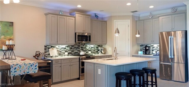 kitchen with stainless steel appliances, light countertops, ornamental molding, a kitchen island with sink, and a sink