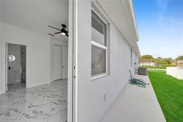 view of side of home with ceiling fan, a yard, and central AC unit