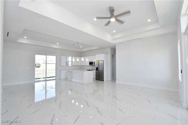 unfurnished living room with a tray ceiling, ceiling fan, and sink