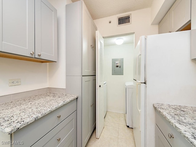 kitchen featuring a textured ceiling, white refrigerator, electric panel, and light stone counters