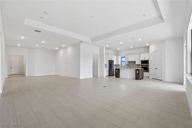 unfurnished living room with visible vents, a raised ceiling, a sink, and recessed lighting