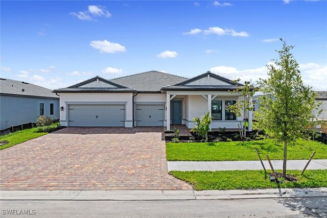 view of front of property with a garage, a tiled roof, decorative driveway, a front lawn, and stucco siding