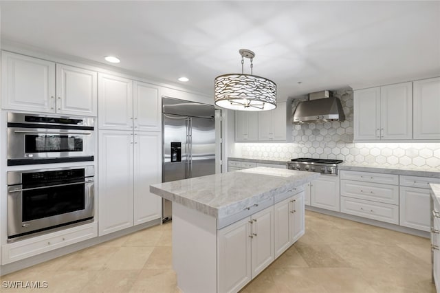 kitchen with stainless steel appliances, wall chimney range hood, decorative light fixtures, white cabinets, and a center island