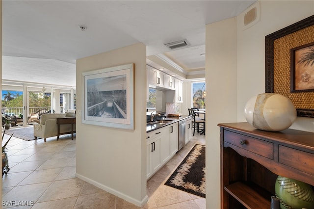 kitchen with light tile patterned flooring, stainless steel dishwasher, sink, and white cabinets