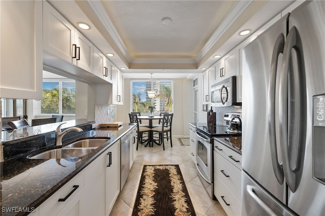 kitchen with sink, appliances with stainless steel finishes, dark stone countertops, a tray ceiling, and white cabinets