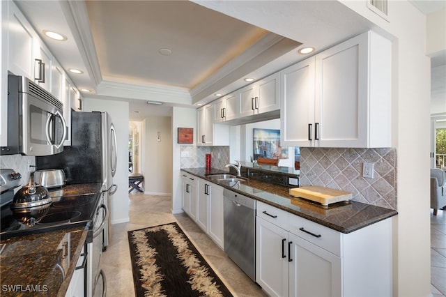 kitchen with appliances with stainless steel finishes, sink, dark stone countertops, white cabinets, and a raised ceiling