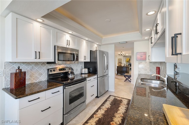 kitchen featuring appliances with stainless steel finishes, sink, white cabinets, dark stone counters, and a tray ceiling