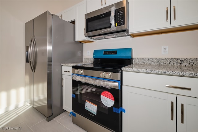 kitchen with light stone counters, white cabinets, light tile patterned flooring, and appliances with stainless steel finishes