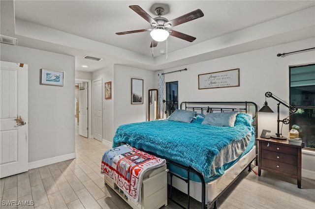 bedroom with ceiling fan, a tray ceiling, and light hardwood / wood-style flooring