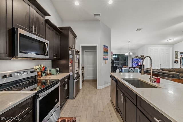 kitchen with pendant lighting, sink, light wood-type flooring, appliances with stainless steel finishes, and a notable chandelier