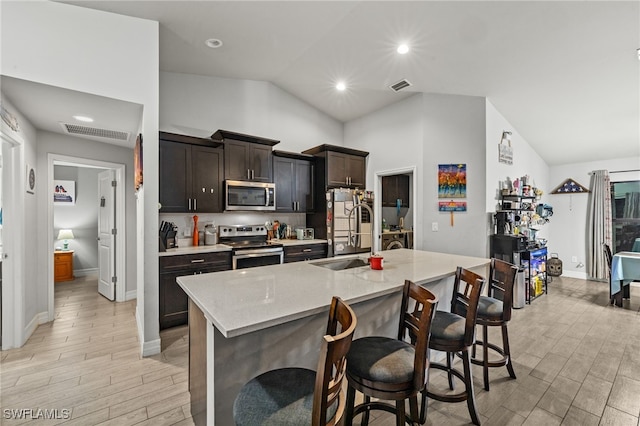 kitchen with sink, a kitchen bar, a kitchen island with sink, appliances with stainless steel finishes, and light wood-type flooring