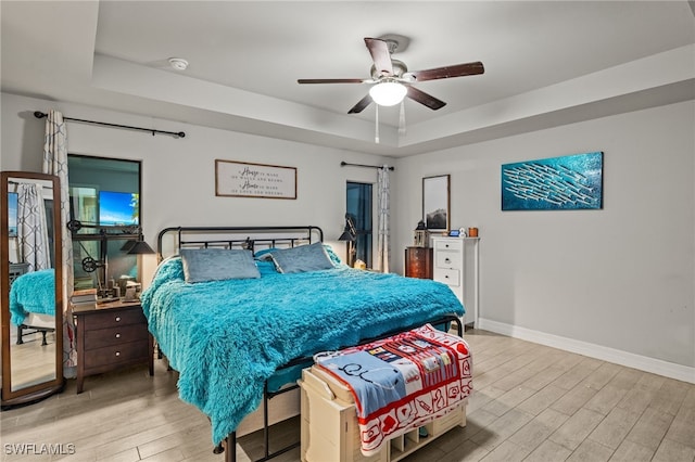 bedroom with ceiling fan, light hardwood / wood-style floors, and a raised ceiling