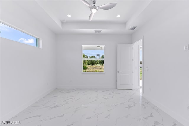 empty room featuring a raised ceiling, ceiling fan, and a healthy amount of sunlight