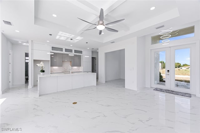 unfurnished living room featuring a tray ceiling, french doors, and sink