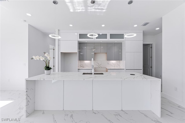 kitchen with backsplash, a center island with sink, sink, gray cabinets, and decorative light fixtures