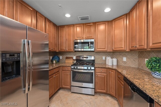 kitchen with decorative backsplash, appliances with stainless steel finishes, light stone counters, and light tile patterned flooring