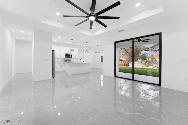 unfurnished living room featuring a tray ceiling, ceiling fan, and sink