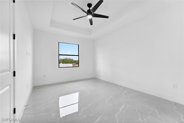 empty room with ceiling fan and a raised ceiling