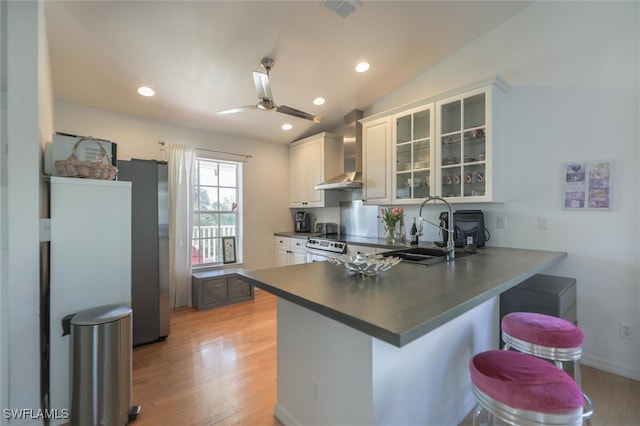 kitchen featuring sink, wall chimney range hood, kitchen peninsula, vaulted ceiling, and white cabinets