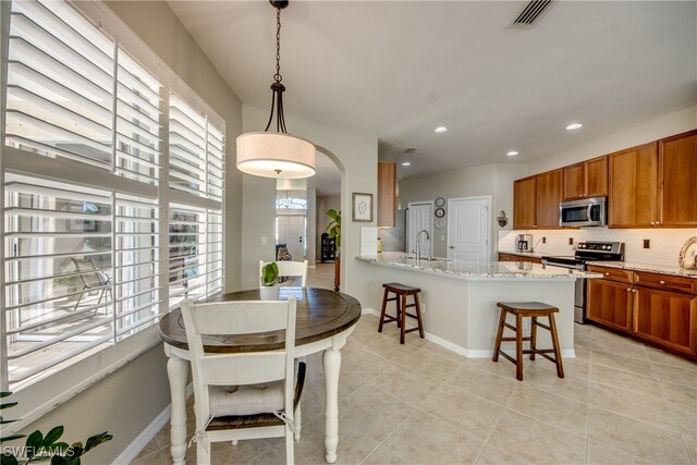 kitchen featuring pendant lighting, backsplash, appliances with stainless steel finishes, light stone counters, and kitchen peninsula