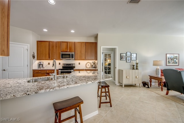 kitchen featuring light stone countertops, appliances with stainless steel finishes, decorative backsplash, sink, and a breakfast bar area