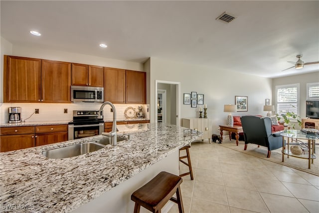 kitchen featuring a kitchen breakfast bar, stainless steel appliances, light stone counters, and sink