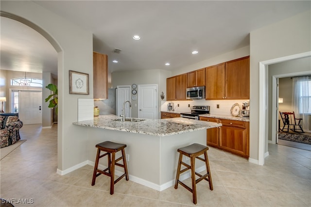 kitchen with sink, stainless steel appliances, light stone counters, a breakfast bar area, and decorative backsplash