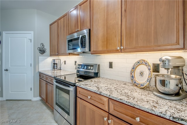 kitchen with backsplash, light stone countertops, light tile patterned floors, and stainless steel appliances