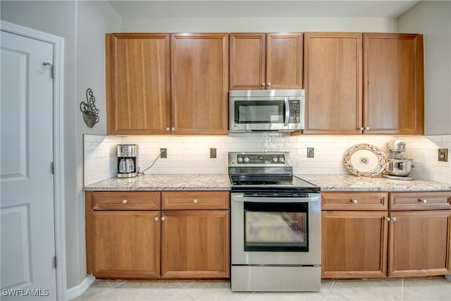 kitchen featuring tasteful backsplash, light stone countertops, light tile patterned flooring, and appliances with stainless steel finishes