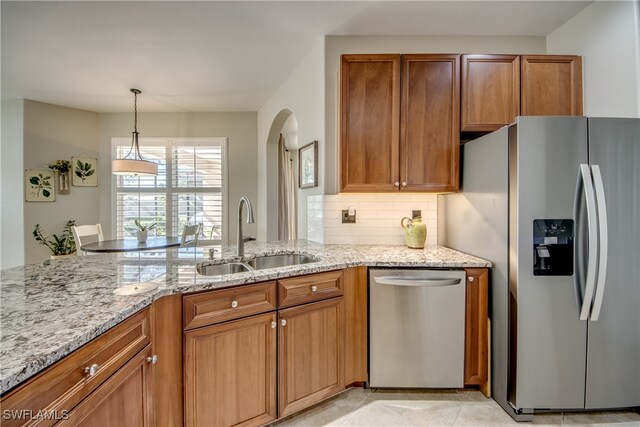 kitchen featuring light stone countertops, appliances with stainless steel finishes, backsplash, sink, and hanging light fixtures