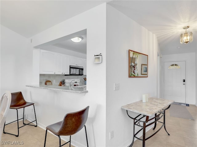 kitchen featuring a breakfast bar, white stove, kitchen peninsula, decorative backsplash, and white cabinetry