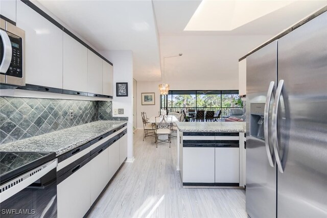 kitchen with white cabinets, pendant lighting, stainless steel appliances, and light hardwood / wood-style flooring