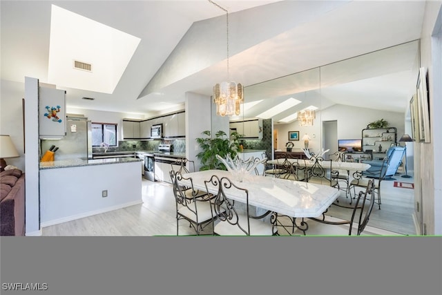 dining area featuring light hardwood / wood-style flooring, lofted ceiling with skylight, and a notable chandelier