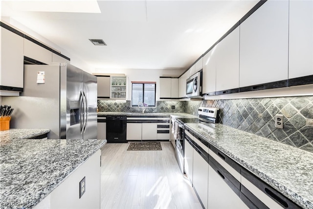 kitchen featuring backsplash, light hardwood / wood-style flooring, light stone countertops, appliances with stainless steel finishes, and white cabinetry