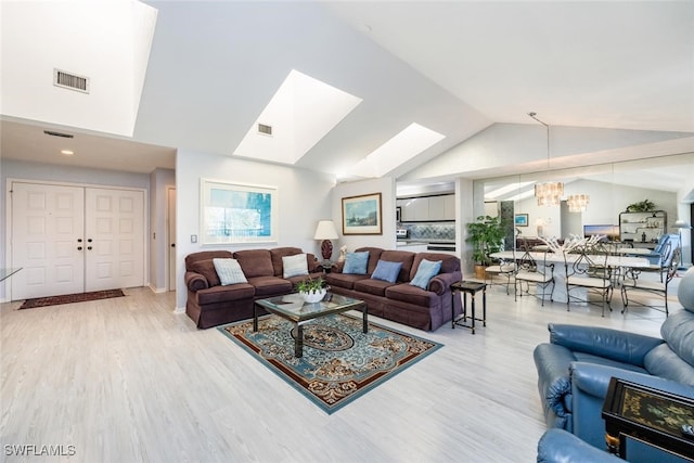 living room with light hardwood / wood-style floors, an inviting chandelier, and vaulted ceiling with skylight