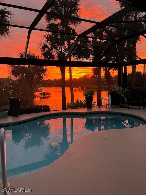 pool at dusk with glass enclosure, a water view, and a patio