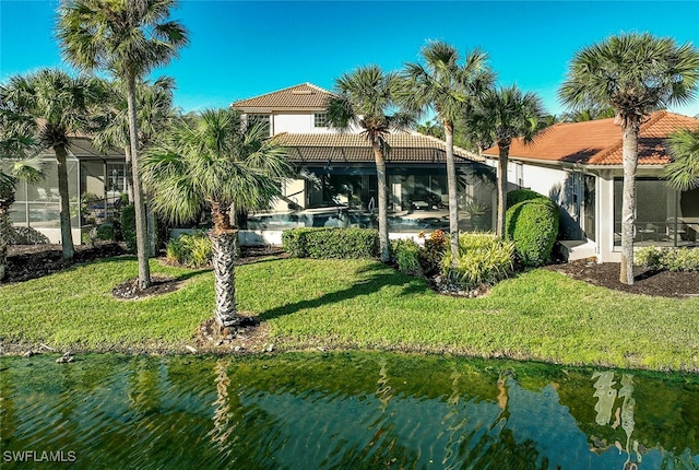 back of house featuring glass enclosure, a yard, and a water view