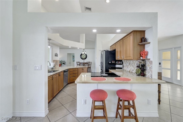 kitchen featuring kitchen peninsula, a kitchen bar, decorative backsplash, light tile patterned floors, and appliances with stainless steel finishes